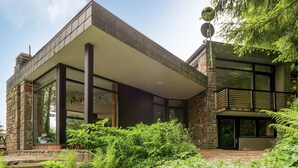 Una casa moderna con fachada de piedra, ventanas amplias y un patio cubierto.
