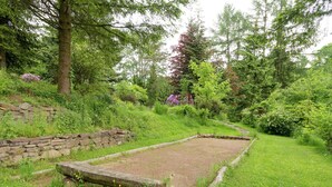 Un jardín con muro de piedra, zona cubierta de césped y diversas árboles y arbustos.