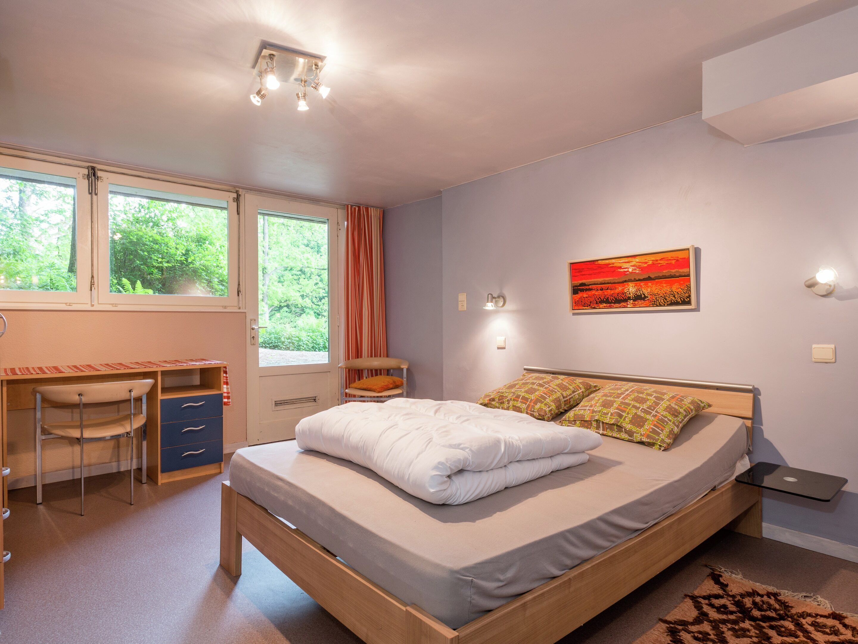 Um quarto com cama, escrivaninha, cadeira e janela com cortinas.