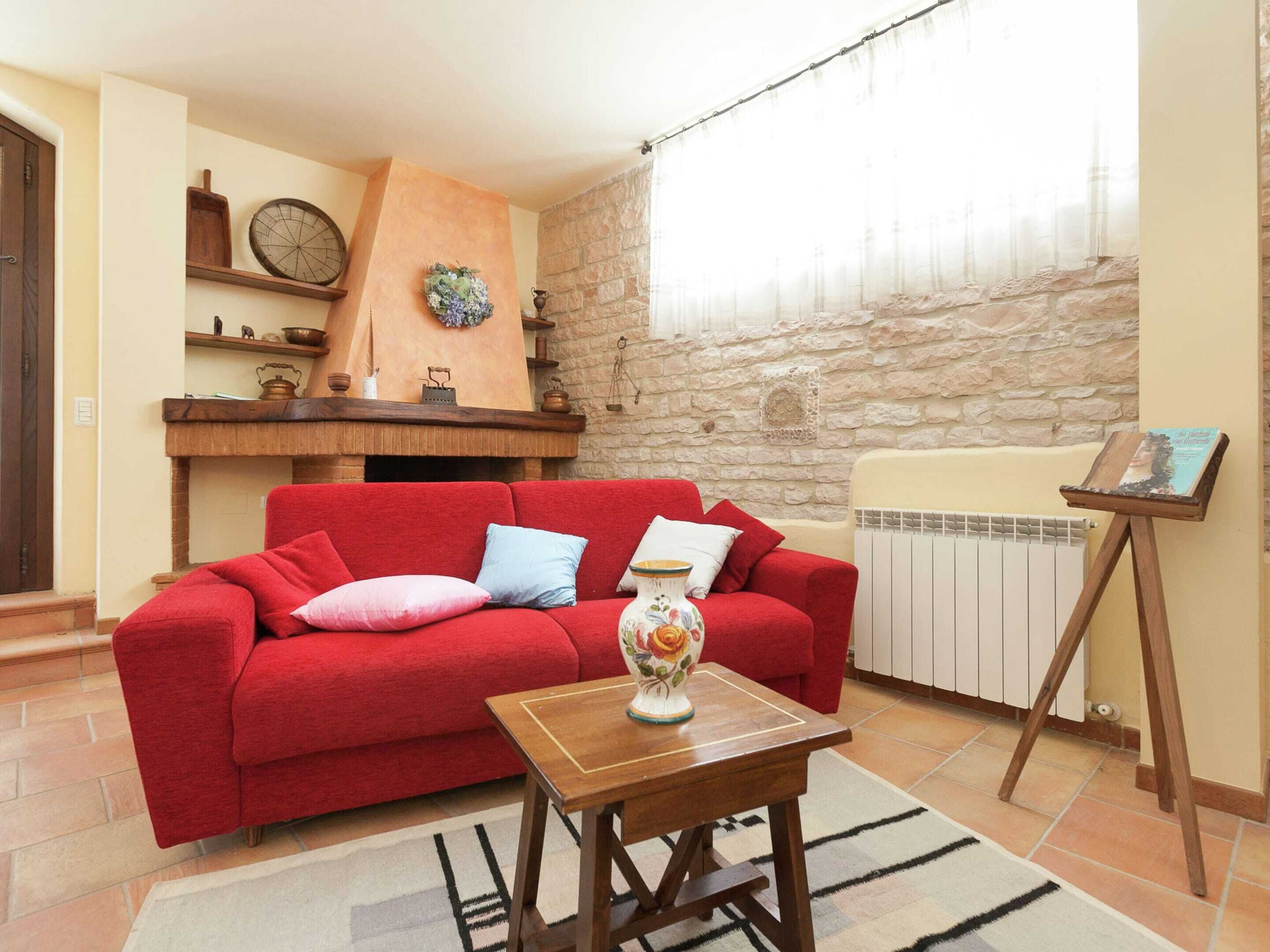 Una sala de estar con un sofá rojo, una mesa de centro de madera, un jarrón decorativo y una pared de piedra.
