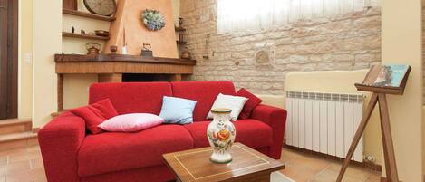 Una sala de estar con un sofá rojo, una mesa de centro de madera, un jarrón decorativo y una pared de piedra.