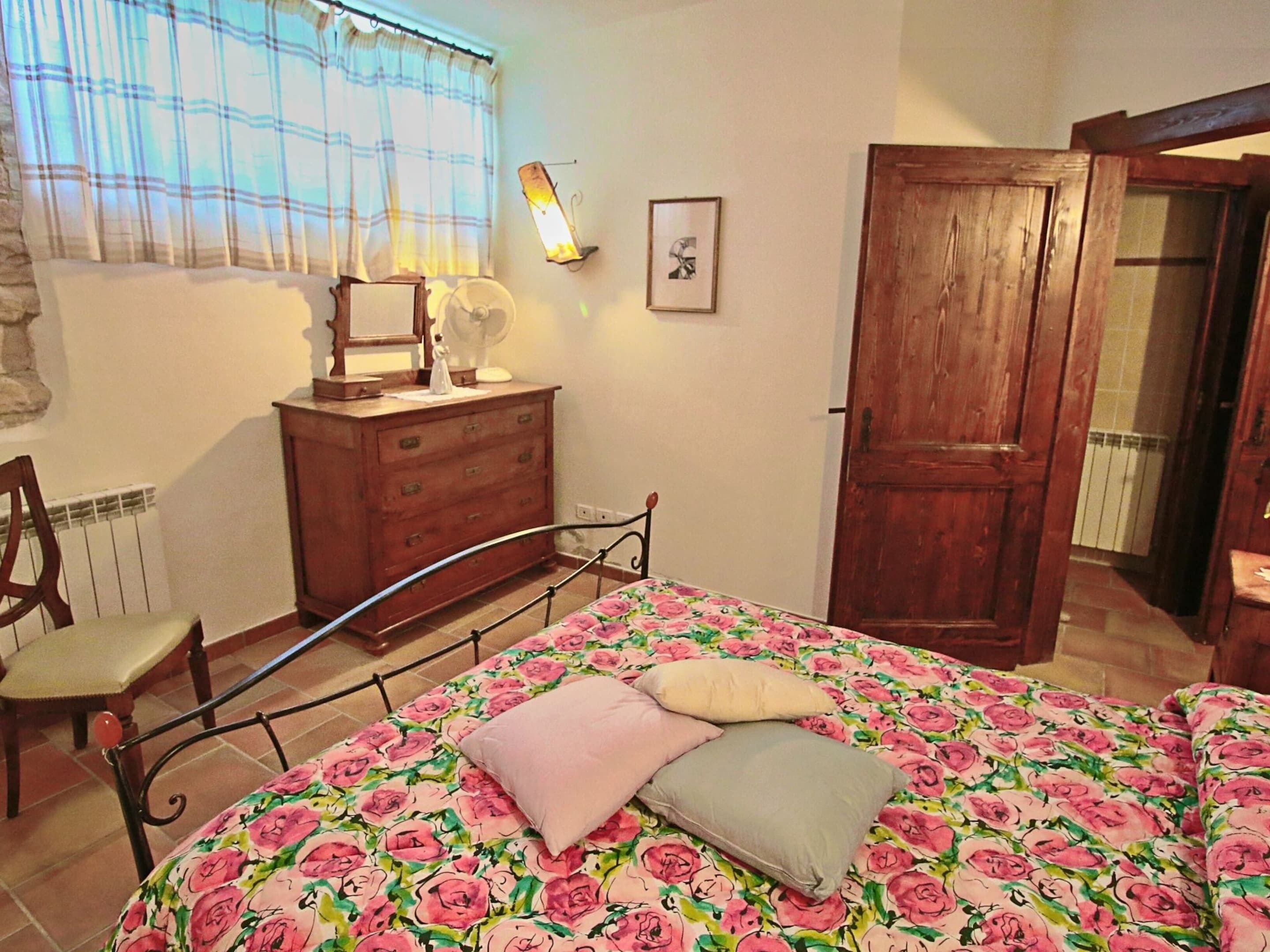 A bedroom with a bed, dresser, chair, and a wooden door.