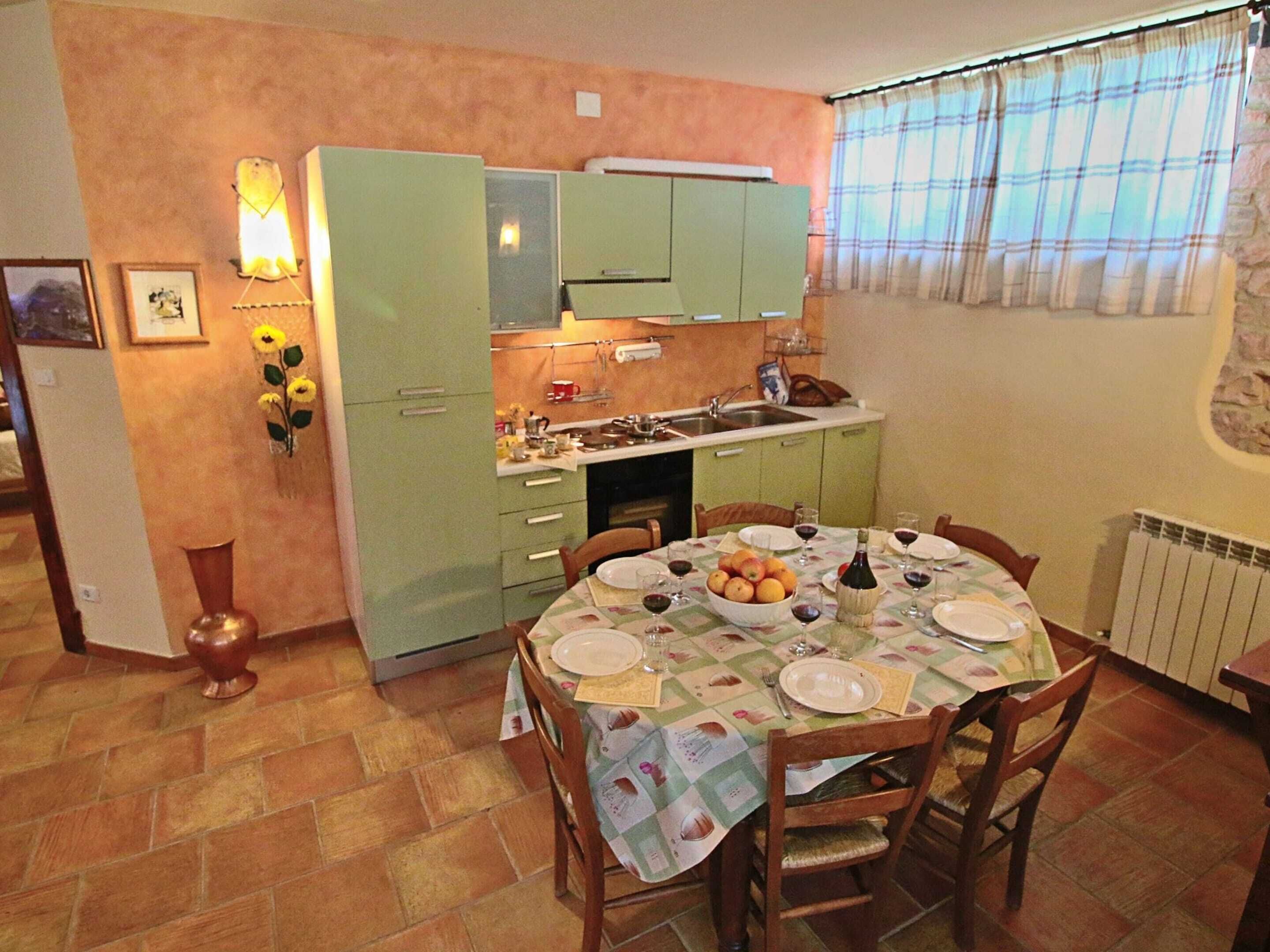 Un coin repas avec une table dressée pour quatre personnes, une cuisine avec des meubles verts et un radiateur fixé au mur.