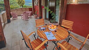 An outdoor patio with a round wooden table, six wooden chairs, and a bowl of fruit and wine glasses. - Family Cottage in Cagli With Pool (Cagli)