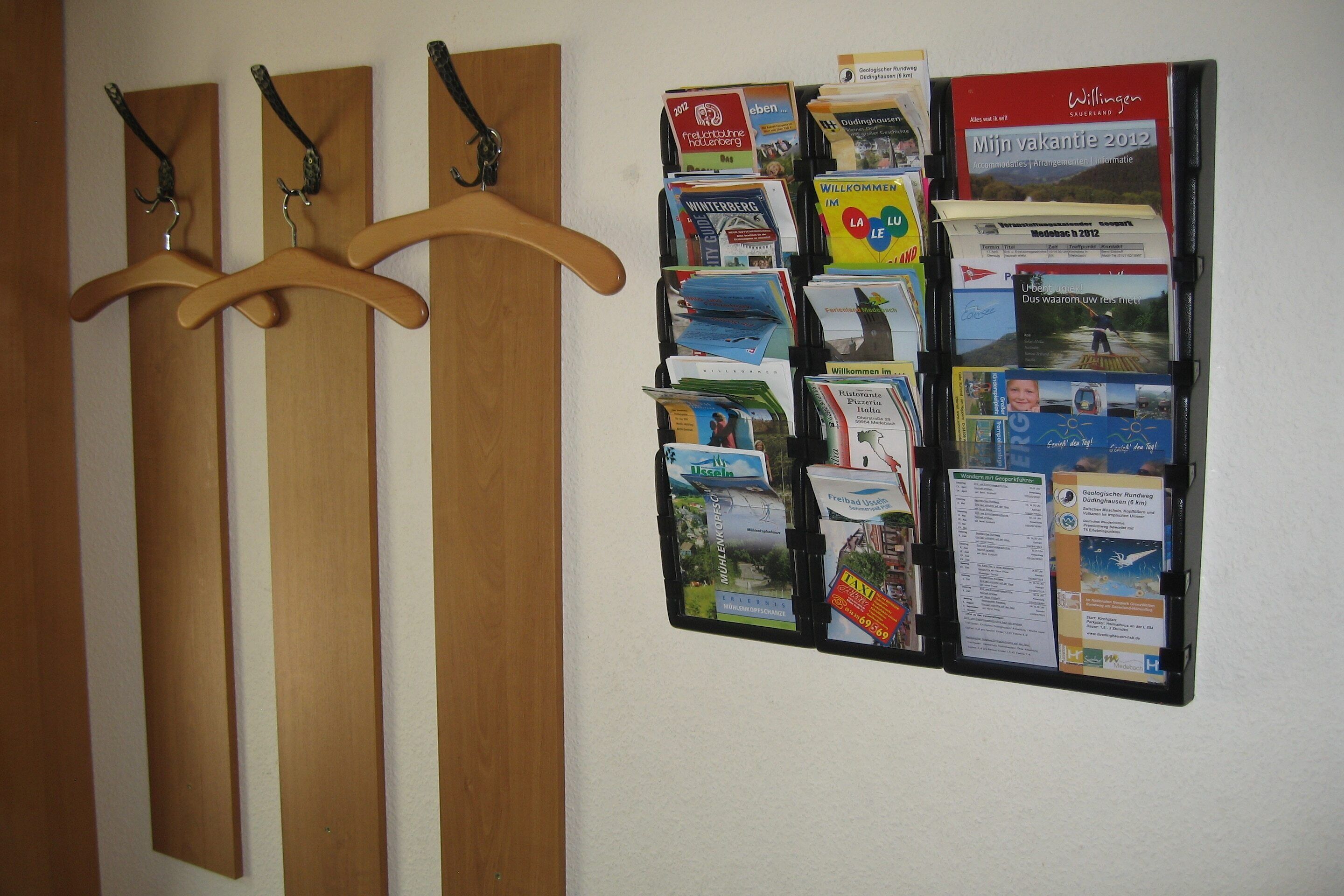 A bulletin board with various travel brochures and a wooden coat rack with hangers.