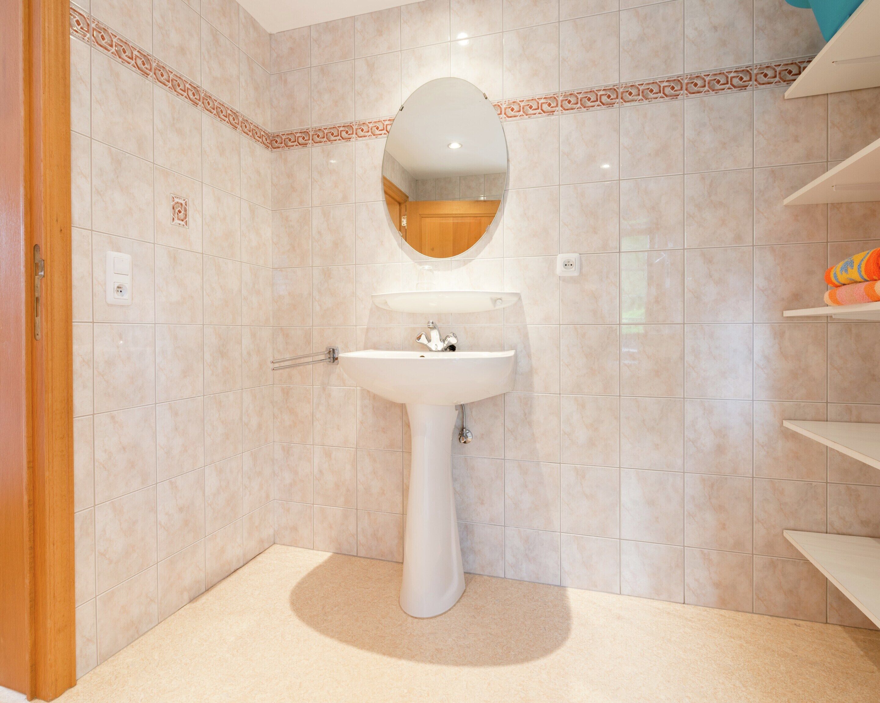 A bathroom with a pedestal sink, a mirror, and a tiled wall.