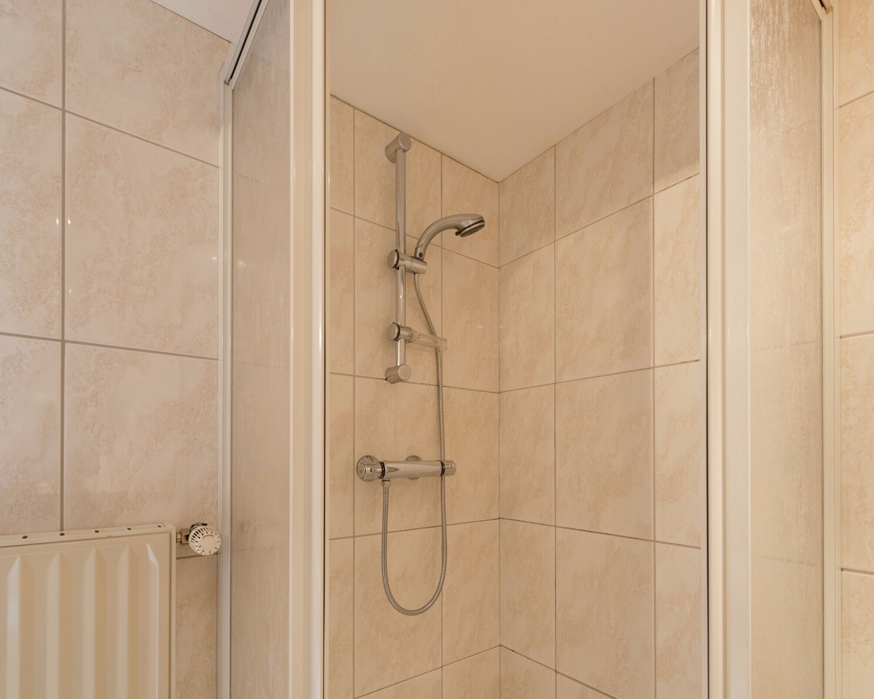 A shower with a handheld showerhead and a fixed showerhead, a control panel, and a tiled wall.