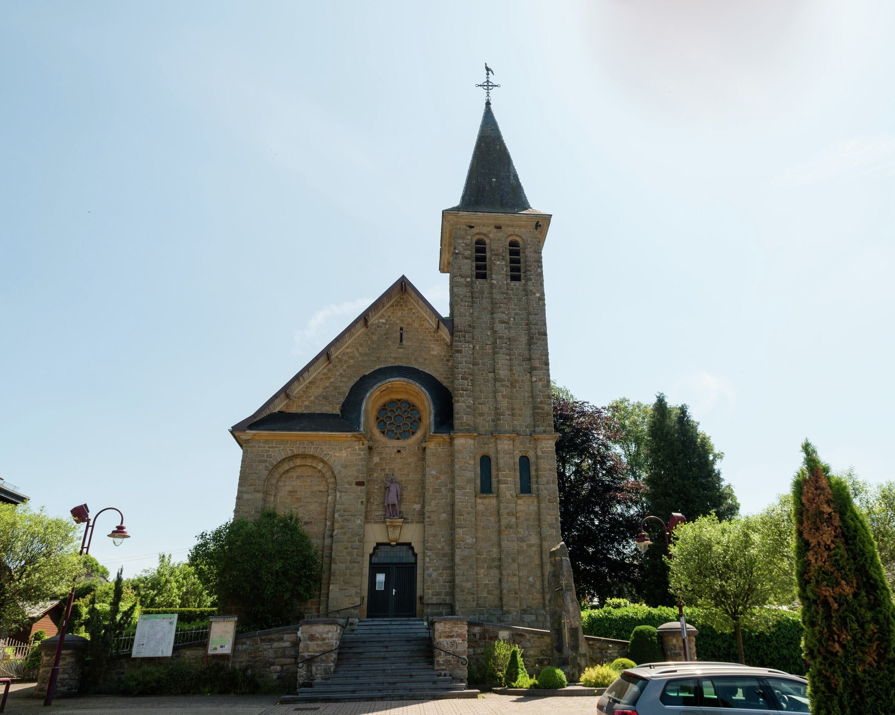 A church with a tall tower, a statue at the entrance, and steps leading up to the door.