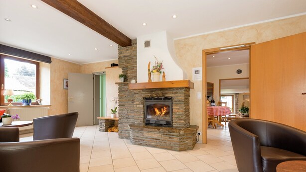 A room with a stone fireplace, leather chairs, a wooden ceiling beam, and a view through an open door. - Holiday Home with Sauna, Garden, Terrace, BBQ & Fireplace (Waimes)