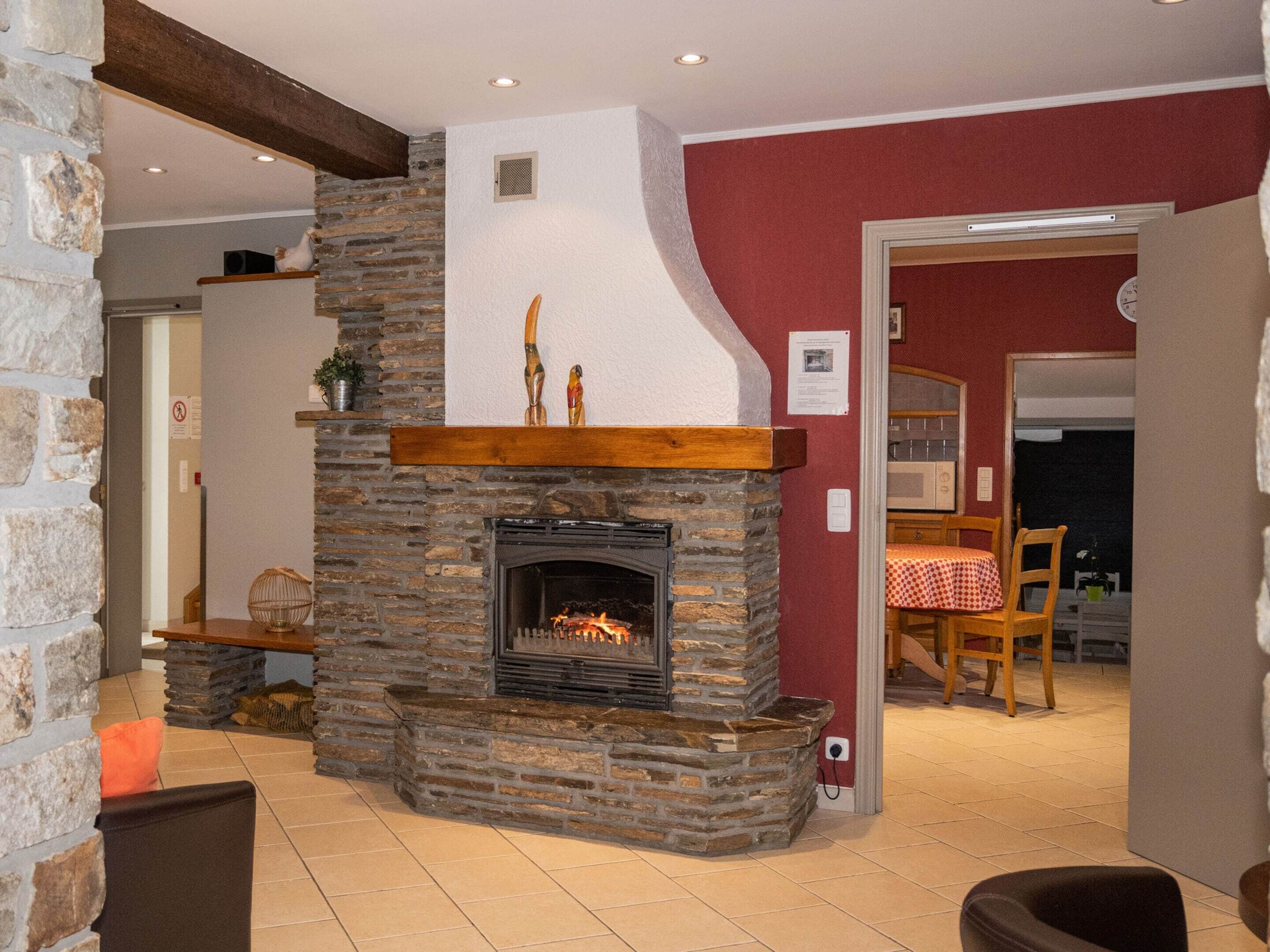 A stone fireplace with a wooden mantel, a tiled floor, and a red wall.