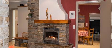 A stone fireplace with a wooden mantel, a tiled floor, and a red wall.