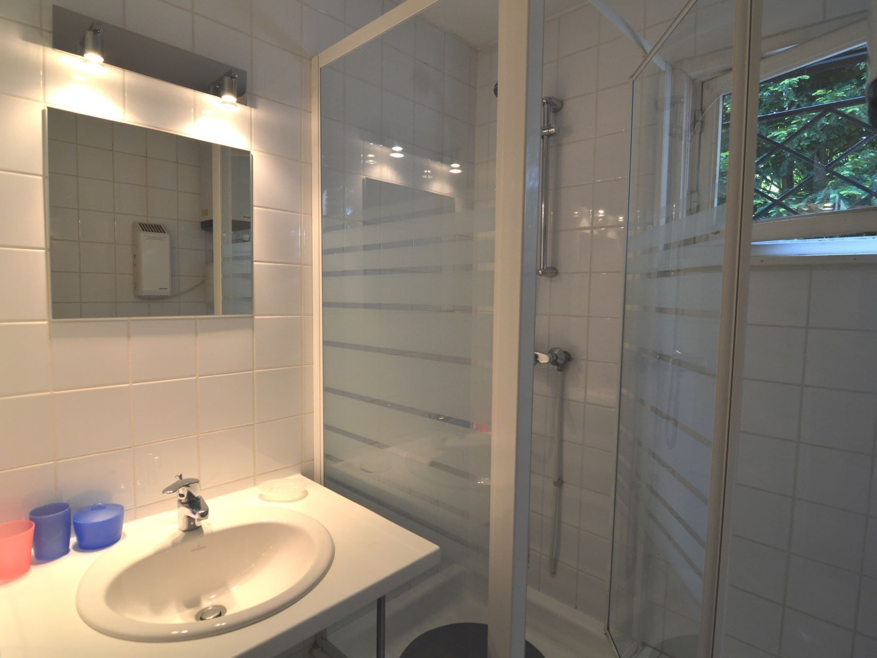 Un baño con lavamanos blanco, espejo y cabina de ducha con mampara de vidrio.