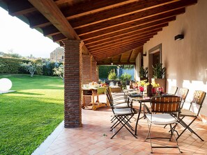 An outdoor patio with a brick column, wooden table, and chairs, surrounded by a well-maintained lawn and a stone wall.