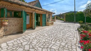 Un camino empedrado que lleva a una edificación rústica con contraventanas verdes y techo de tejas.
