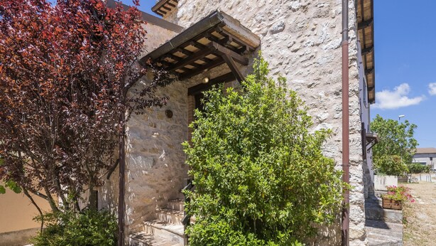 A stone building with a wooden staircase leading to a covered entrance. - Belvilla by OYO Fonni Blu (Sellano)