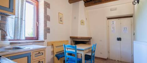 Una pequeña cocina con una mesa y sillas de madera, una ventana con cortinas, y una puerta con señalización de COVID-19.