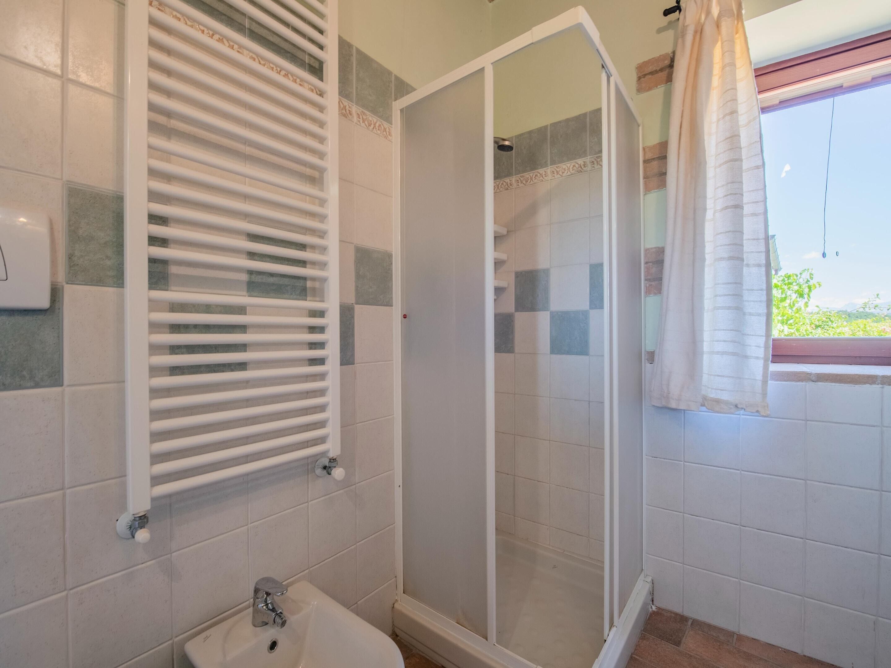 A bathroom with a shower, a sink, and a window with a curtain.