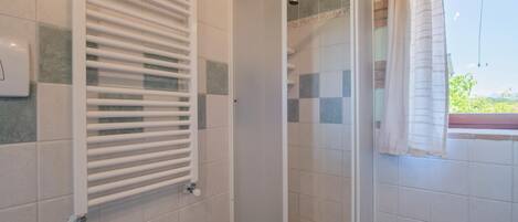 A bathroom with a shower, a sink, and a window with a curtain.