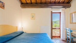 A bedroom with a bed, a desk, and a balcony with a view. - Belvilla by OYO Fonni Blu (Sellano)