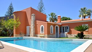 A swimming pool with a stone wall and a palm tree in the background. - Villa in Quiet Area with Private Pool near Golf Courses & Marina (Loulé)