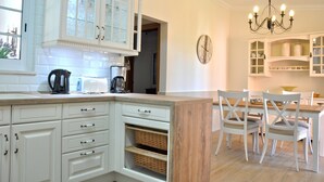 A kitchen with white cabinetry, a wooden island, and a dining area with white chairs and a chandelier. - Villa in Quiet Area with Private Pool near Golf Courses & Marina (Loulé)