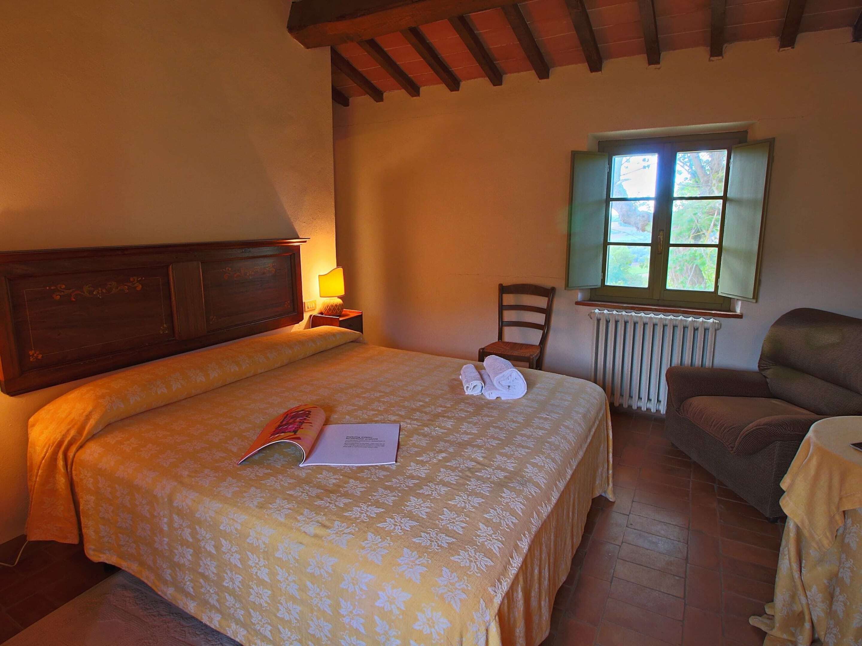 A bedroom with a bed, a chair, a table, a window, and a radiator.