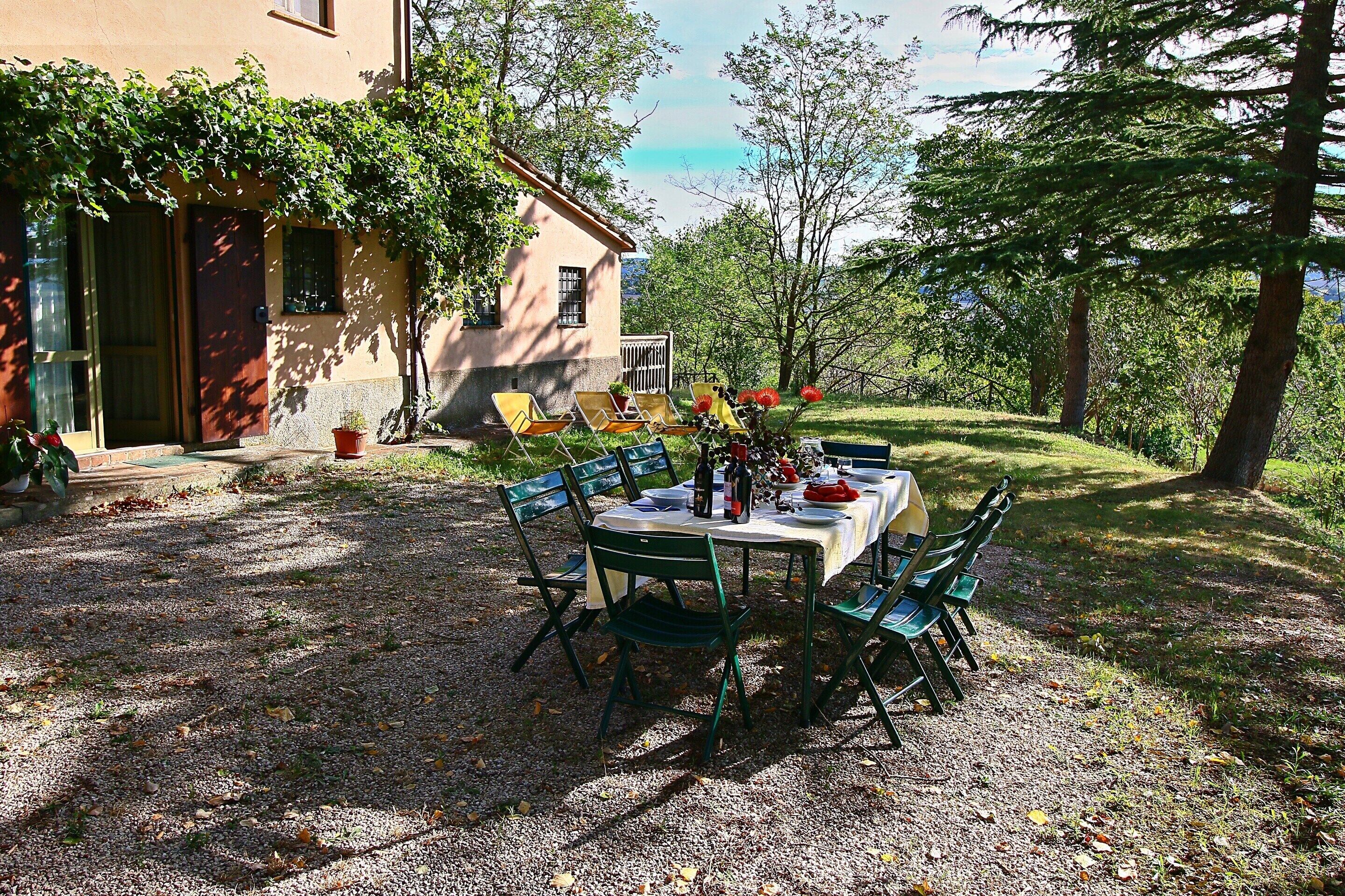 An outdoor dining area with a table and chairs, surrounded by trees and a building.