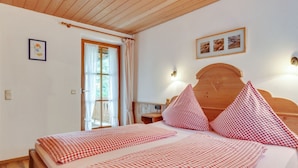 Un dormitorio con cabecera de madera, cama con ropa de cama a cuadros, ventana con cortinas y una lámpara fijada a la pared.