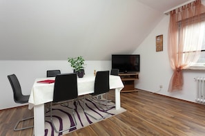 A dining area with a table, chairs, a potted plant, a television, and a window with curtains. - Holiday Home With Garden in Wildemann Germany (Clausthal-Zellerfeld)