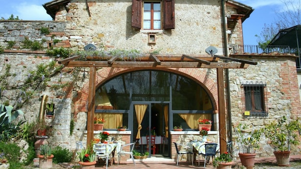 A rustic stone building with a large arched entrance, outdoor seating area, and potted plants. - Elegant Villa in Tuscany (Rapolano Terme)
