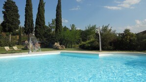 A clear blue swimming pool with lounge chairs and tall trees in the background. - Elegant Villa in Tuscany (Rapolano Terme)