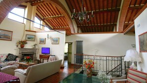 A spacious living room with a fireplace, a television, and a staircase leading to an upper level. - Elegant Villa in Tuscany (Rapolano Terme)