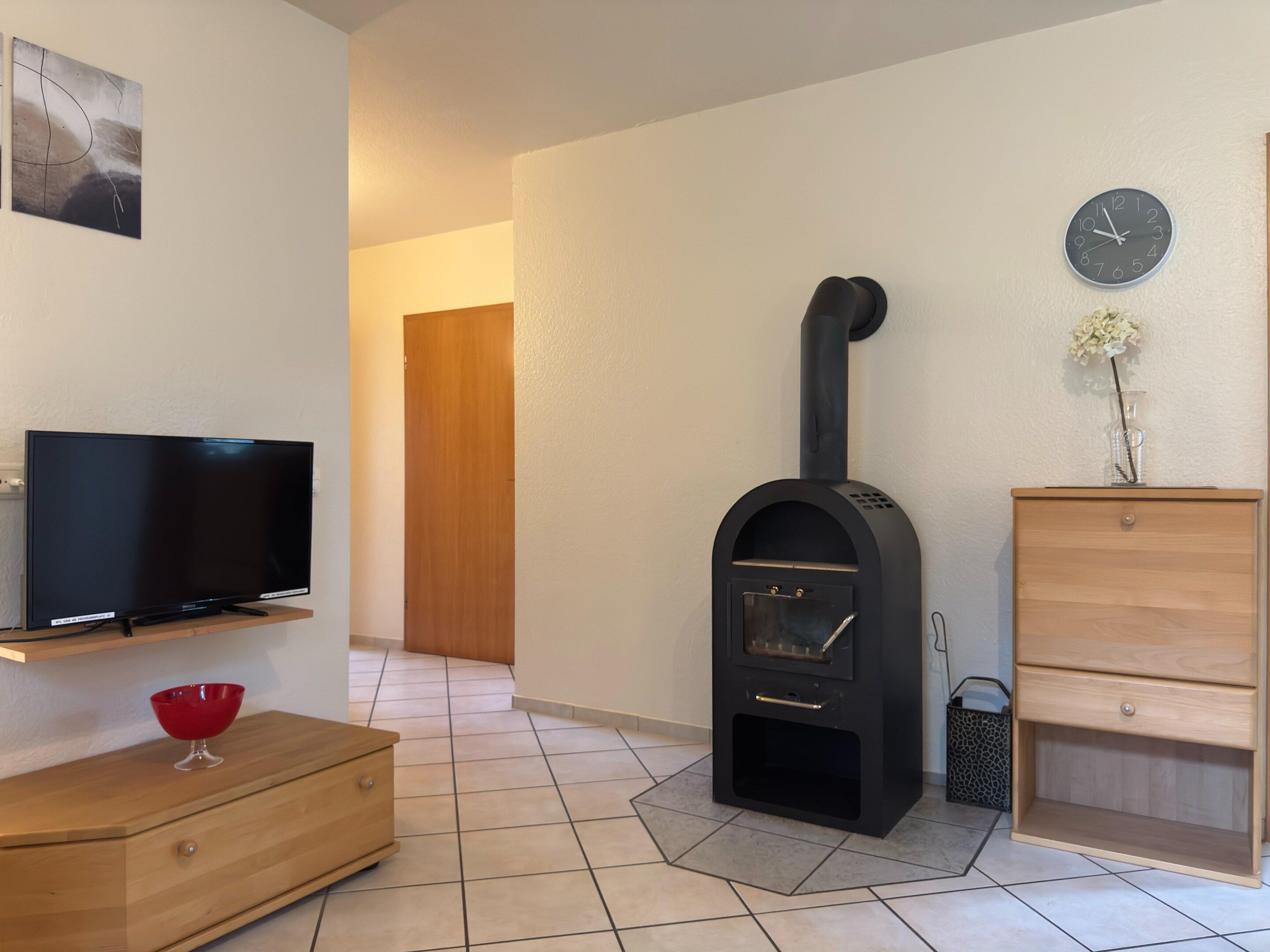 Una sala de estar con televisor, un mueble de madera, un estufa de leña negra y un reloj en la pared.