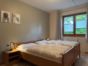 A bedroom with a wooden bed, a bedside table with a lamp, and two wall-mounted artworks.
