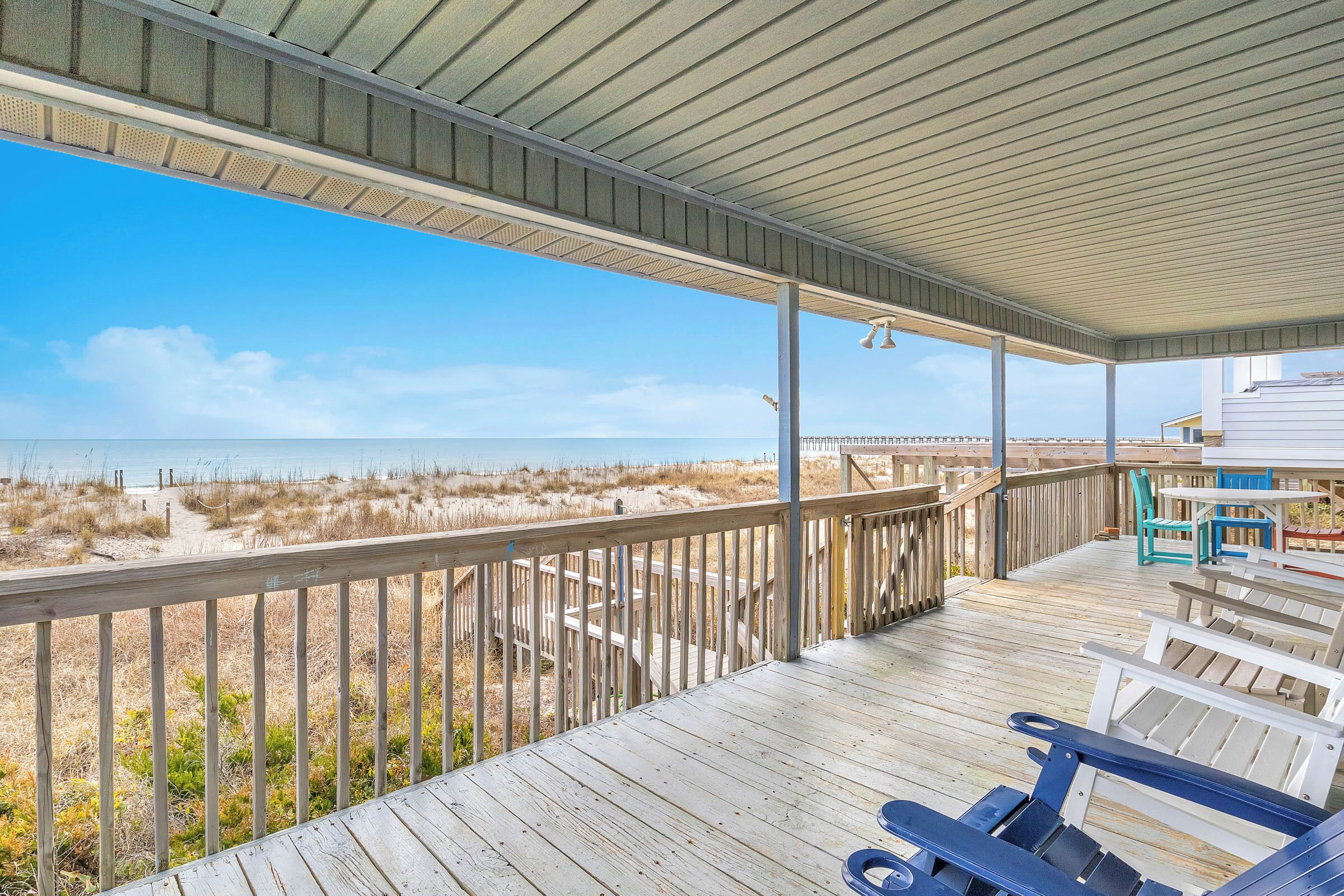 Eine überdachte Terrasse mit Blick auf den Strand, Holzstühle und ein Tisch.