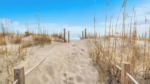 A sandy beach path with wooden posts and ropes, leading to the sea.