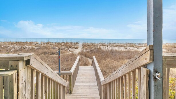 A wooden boardwalk leading to a beach with a clear sky.