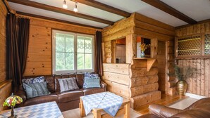 Ein gemütliches Blockhaus-Interieur mit einem braunen Ledersofa, einem Holztisch mit kariertem Tischläufer und einem Fenster mit Vorhängen.