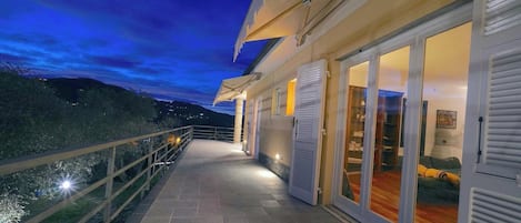A balcony with a railing, a door with shutters, and a view of the landscape.
