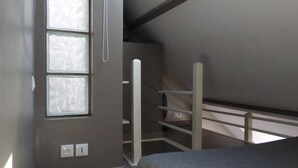 A small, dimly lit room with a single bed, a window, and a slanted ceiling.