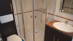 A bathroom with a glass-enclosed shower, a white toilet, and a sink with a wooden countertop.