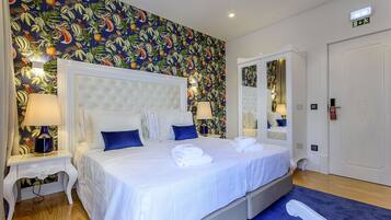 Una habitación de hotel con una cama grande, ropa de cama blanca y un diseño de papel tapiz tropical.