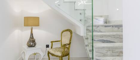 A modern interior with a marble staircase, a gold chair, and a lamp on a white pedestal.