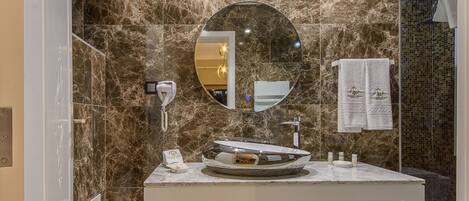 A bathroom with a marble wall, a round mirror, a sink with a vessel basin, and a towel rack with towels.
