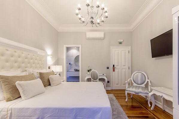 Een hotelkamer met een groot bed, een kroonluchter, een televisie en een zichtbare badkamer door een open deur.
