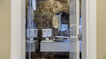 Un baño moderno con pared de mármol, un espejo redondo y un lavabo blanco.