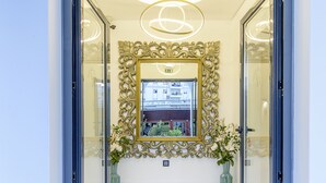 Un pasillo con un espejo grande y ornamentado, dos plantas en macetas y una lámpara en el techo.