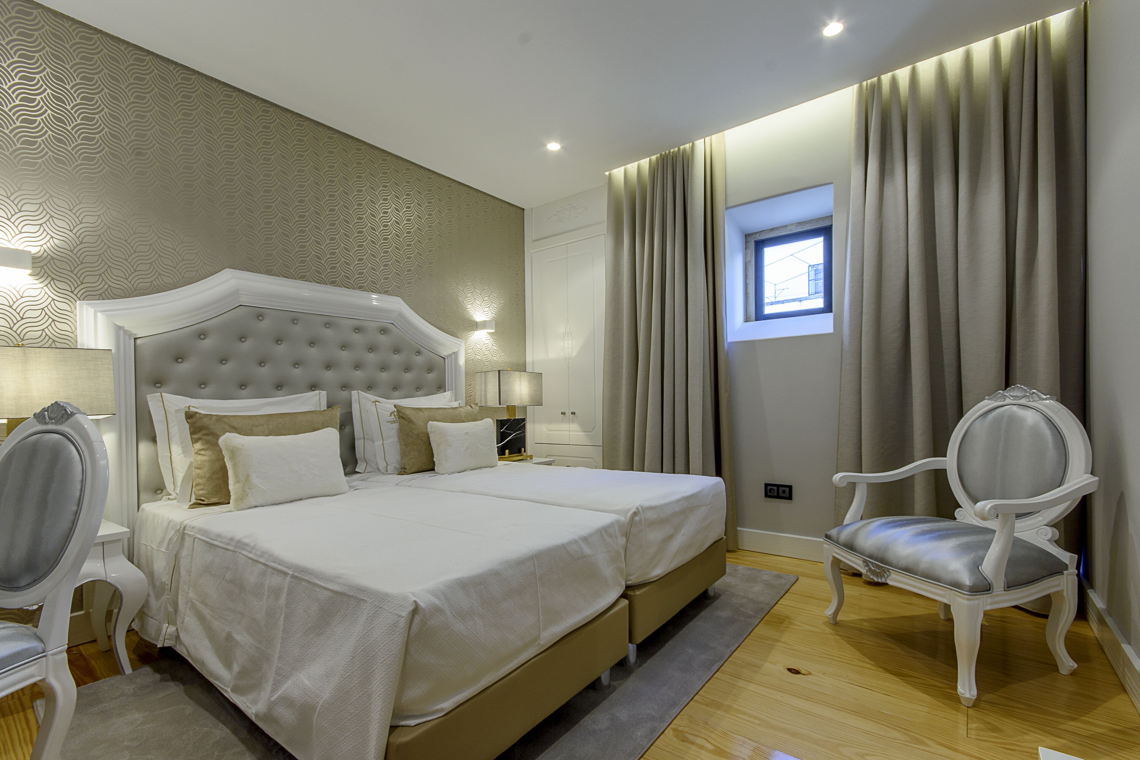 Een hotelkamer met een groot bed, twee nachtkastjes, een stoel en een raam met gordijnen.