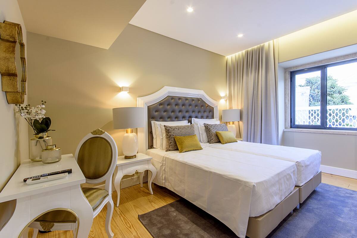 A hotel room with a large bed, bedside lamps, a desk with a chair, and a window with curtains.