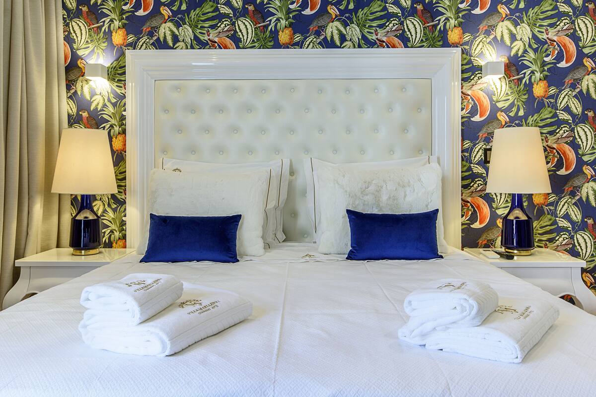 A hotel room with a tufted headboard, two blue pillows, two white towels, and two lamps on nightstands.